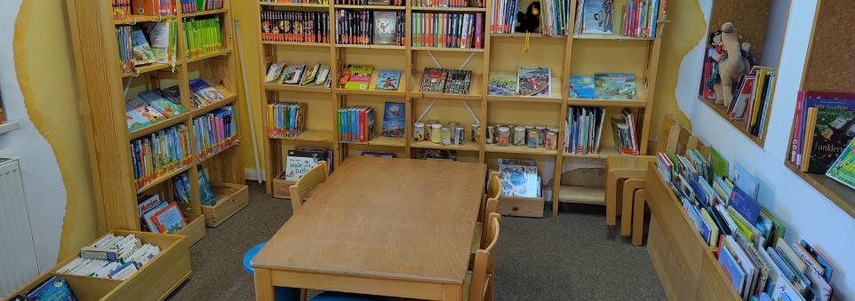 Kinderlesetisch mit Kinderbuchregalen im Hintergrund