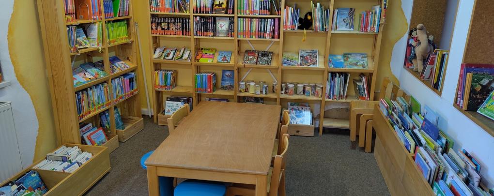 Kinderlesetisch mit Kinderbuchregalen im Hintergrund